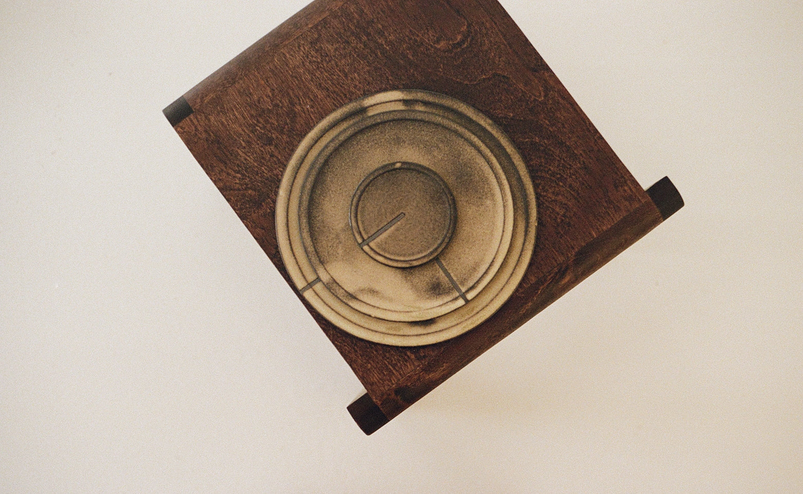 Top down photo of a ceramic plate and small dish on a wooden stool, set against a light background.